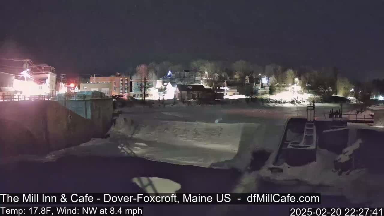 A nighttime view of a snow-covered town beside a partially frozen river under a clear, dark sky.