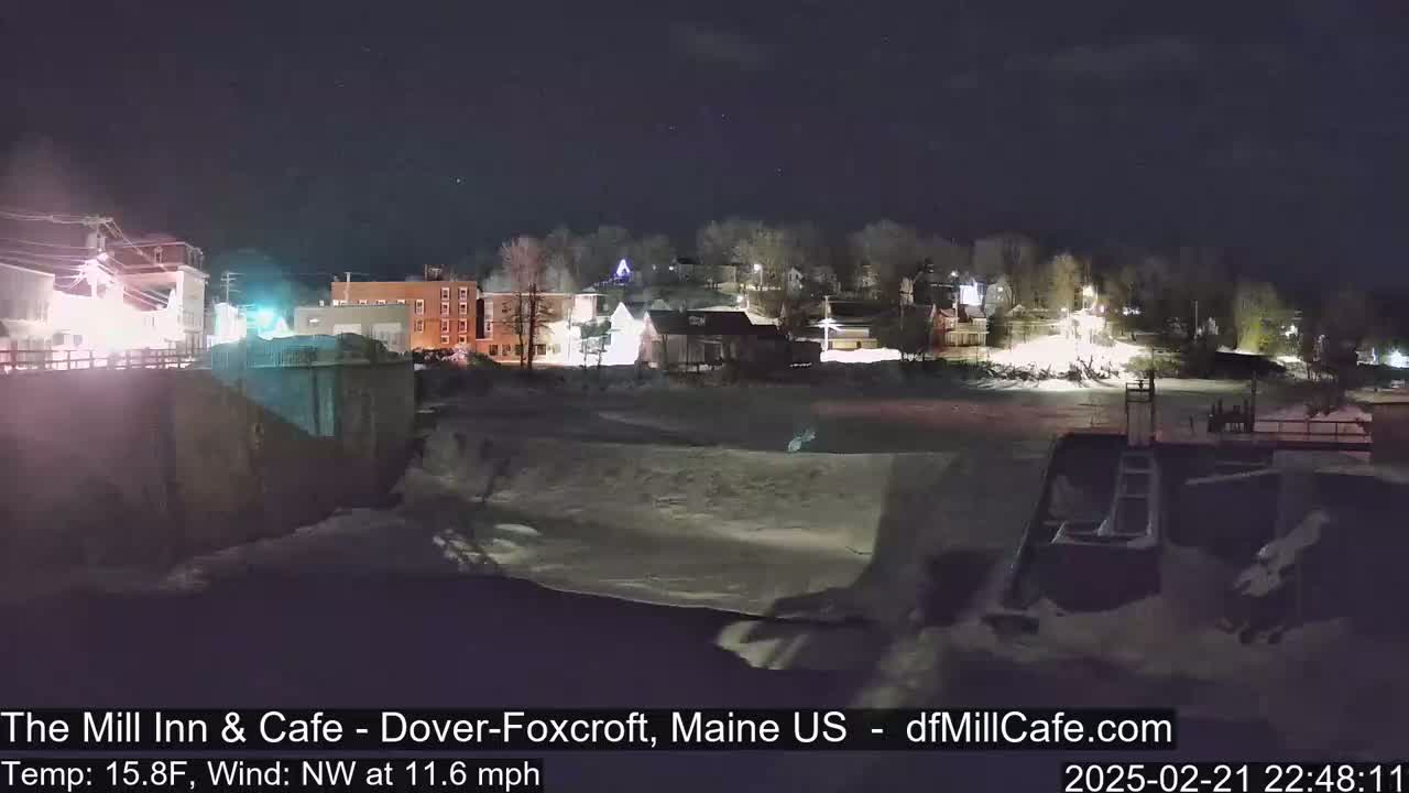 A snow-covered town at night is seen from across a frozen river under a clear, dark sky.