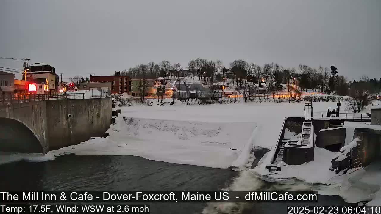 A snow-covered dam and river are seen in a town under a gray sky.