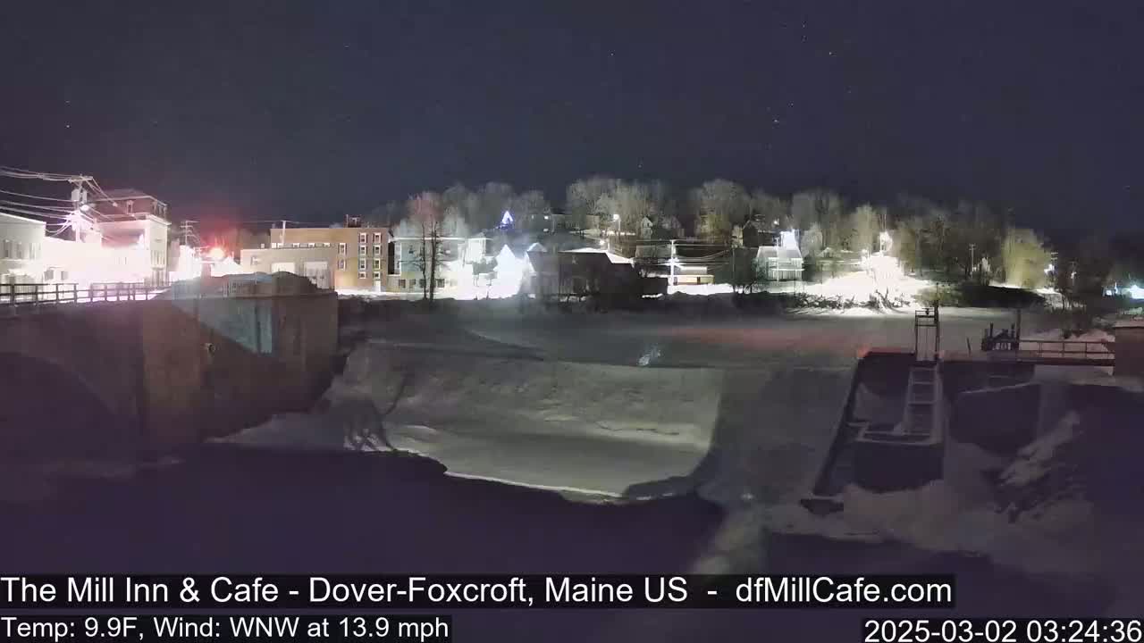 A nighttime view of a snow-covered town beside a partially frozen river, under a clear, starry sky.