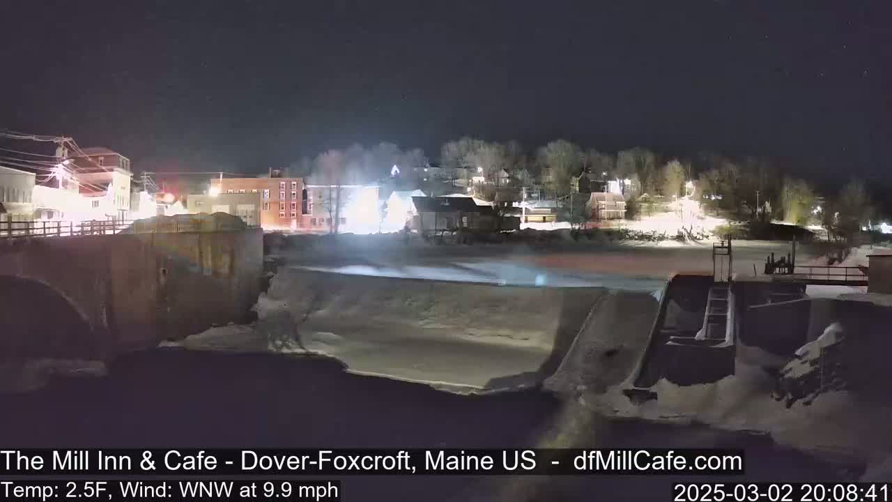A nighttime view of a snow-covered town with a river and dam, under a clear sky.