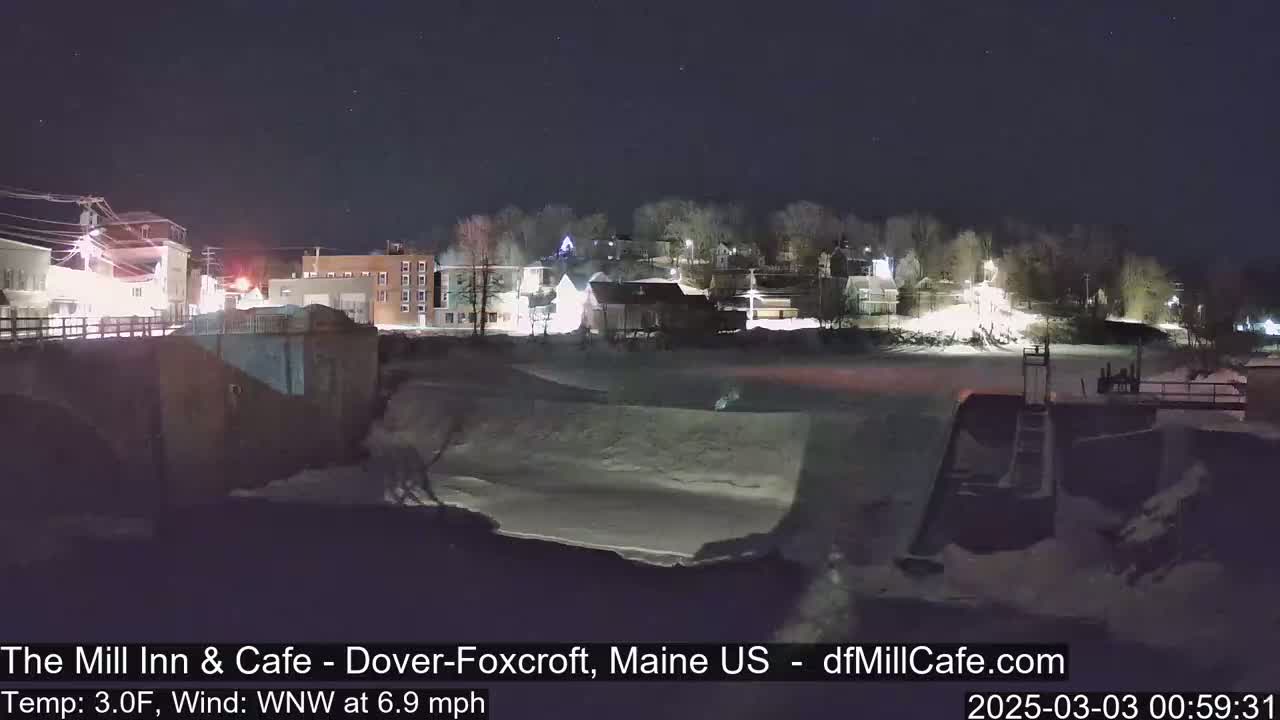 A nighttime view of a snow-covered town by a river, under a clear, dark sky.
