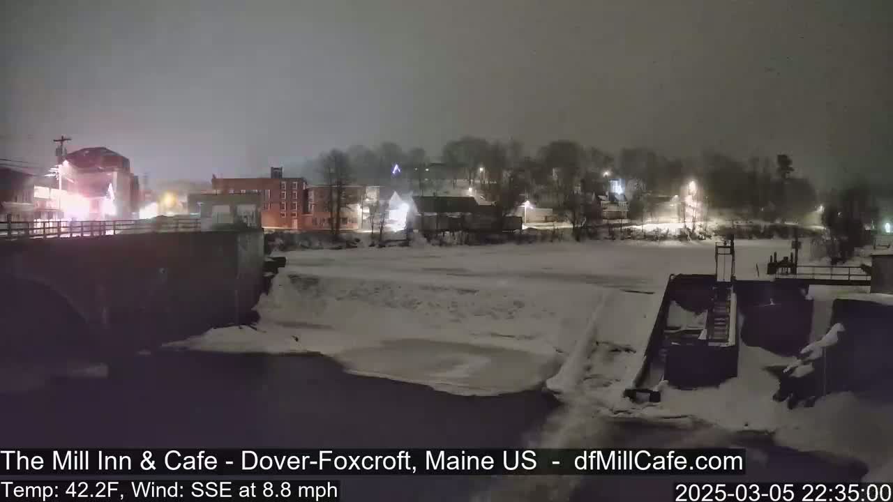 A snow-covered river flows past a small town at night under a gray sky.