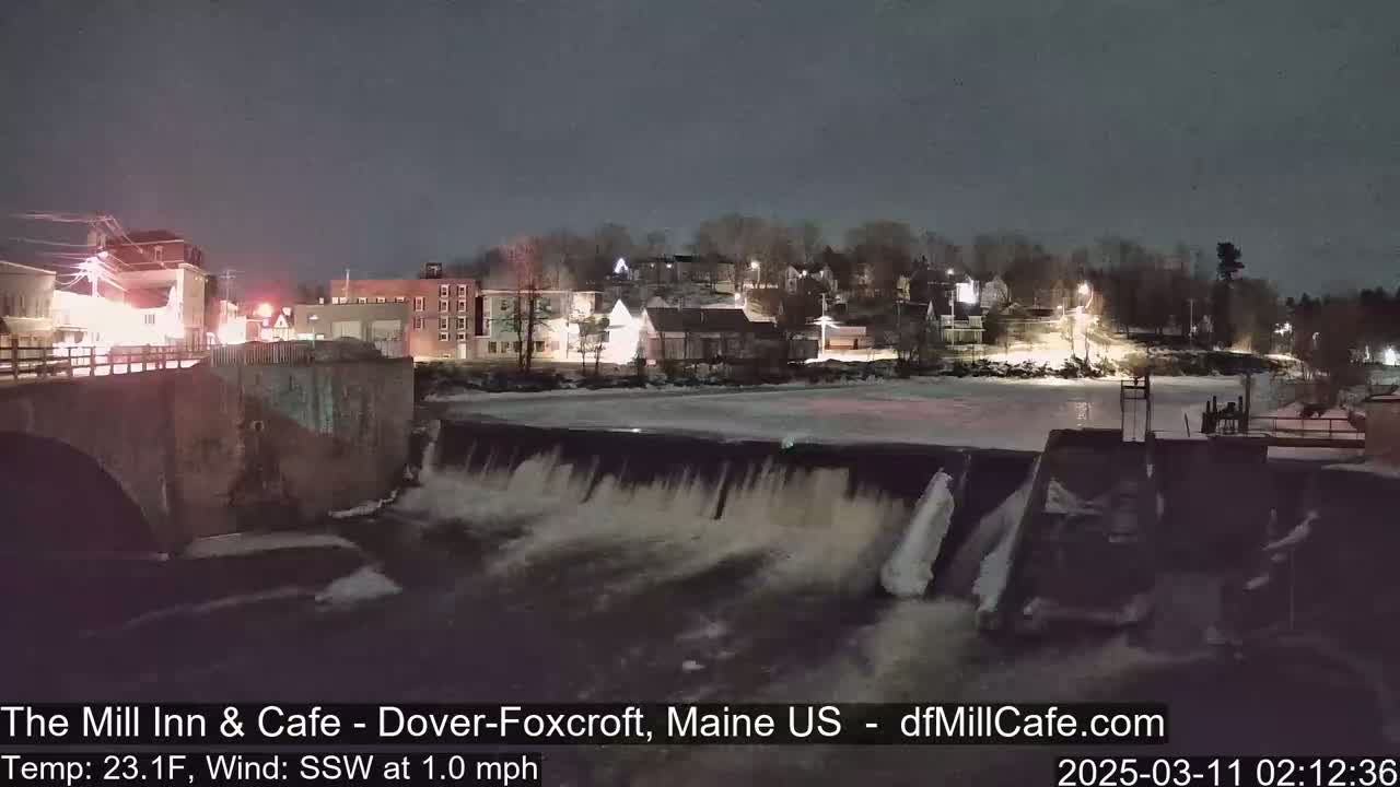 A nighttime view of a dam and river flowing through a town under a dark sky.