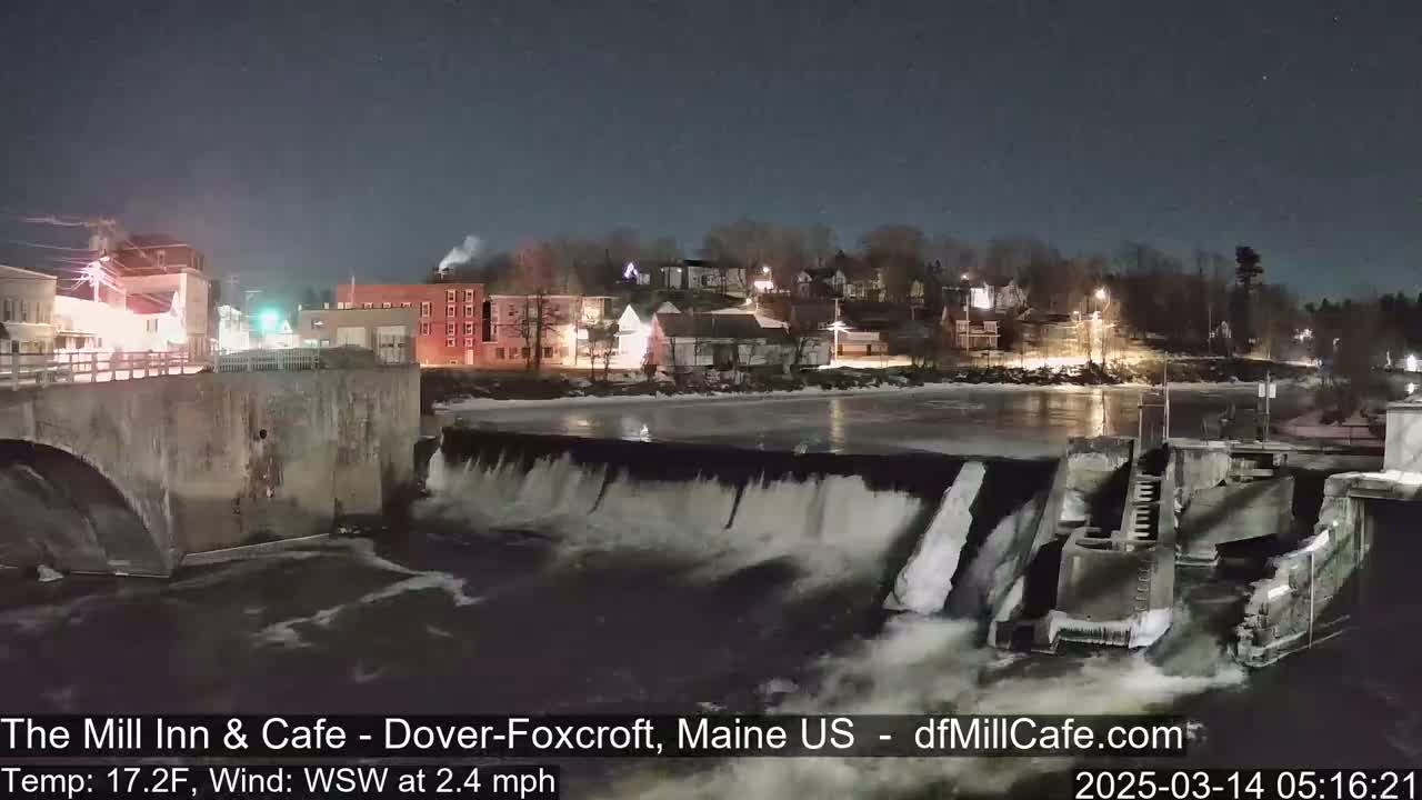 A night scene shows a dam and river flowing past a small town under a clear, dark sky.
