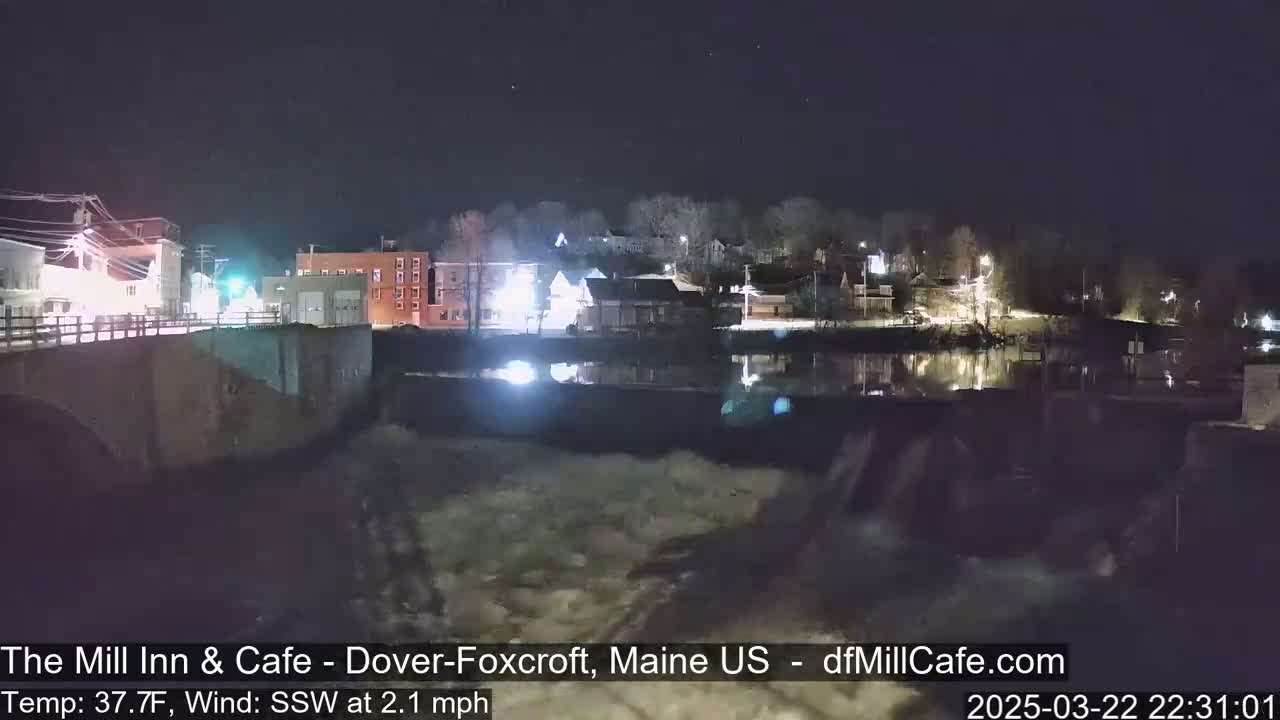 A nighttime view of a town across a river with a dam, under a clear, dark sky.