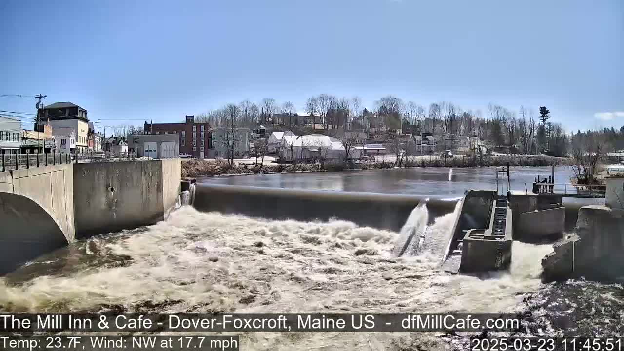 Water rushes over a dam in front of a small town on a clear, windy day.