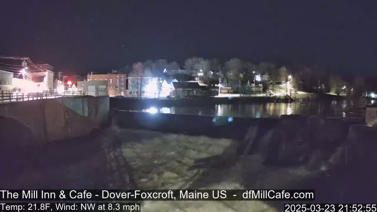 A nighttime view of a town beside a river with a dam, under a clear sky with a northwest wind.
