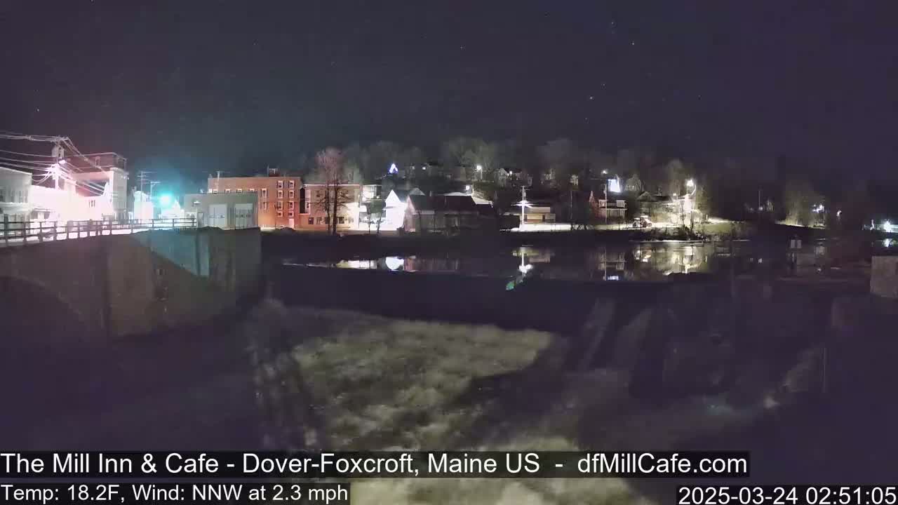 A nighttime view of a town reflecting on a calm river, under a clear, starry sky.
