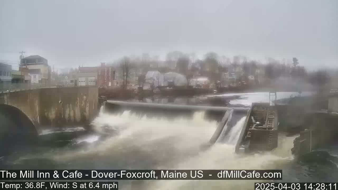 Water rushes over a dam in a foggy, overcast town.