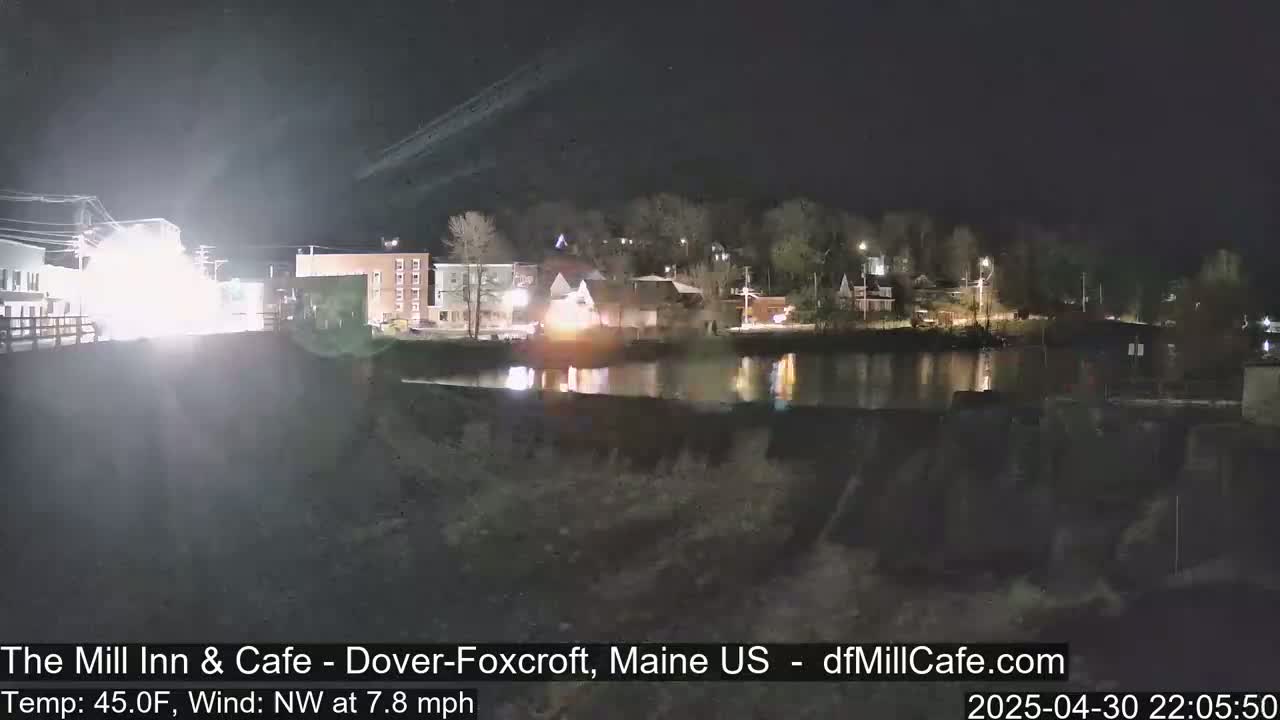 A nighttime view of a calm body of water reflecting lights from buildings across the shore, under a clear, dark sky.