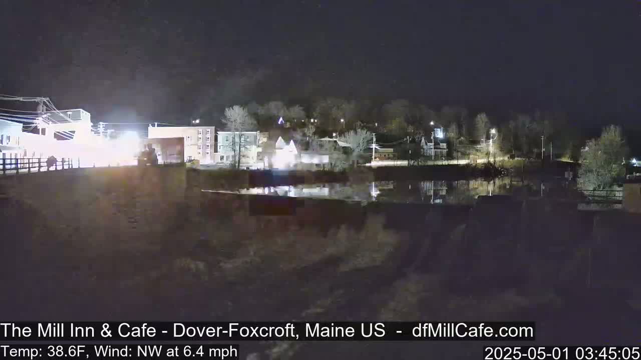 A nighttime view of a calm body of water reflecting the lights of a small town under a clear, dark sky.