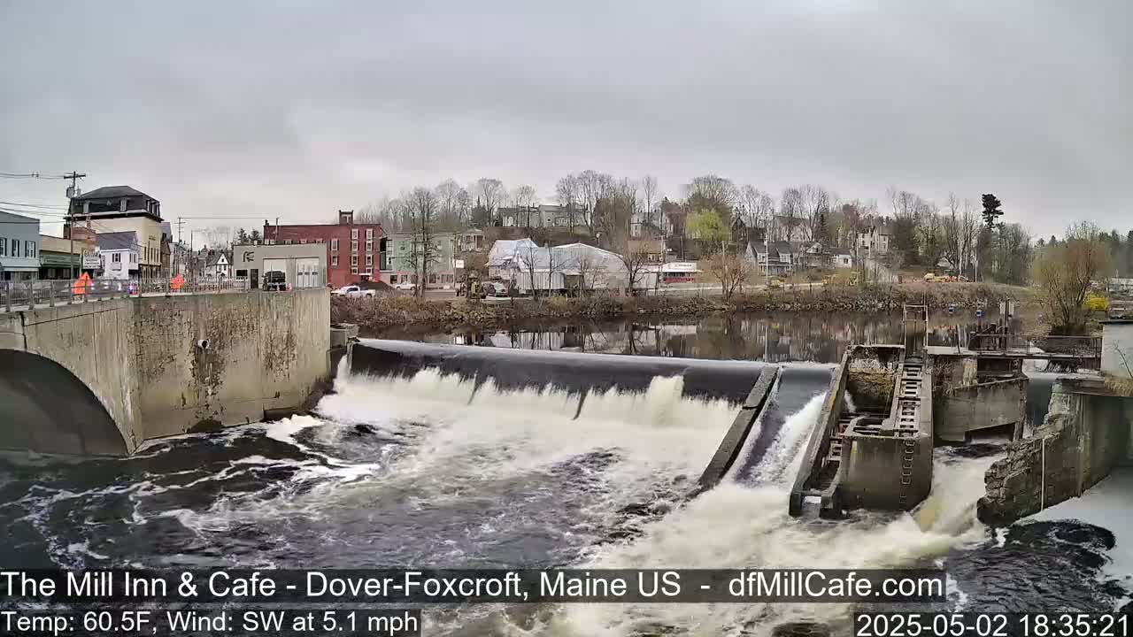 Water flows over a dam in front of a small town on an overcast day.