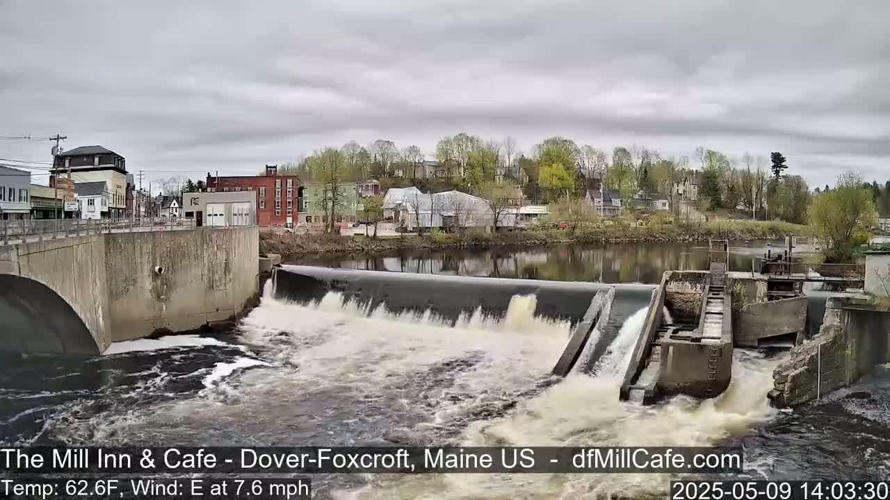 Water flows over a dam in a town with overcast skies.