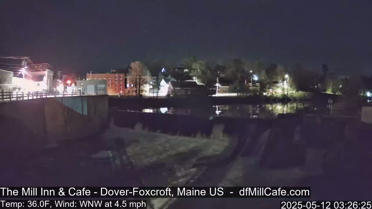 A nighttime view of a town across a calm body of water, seen from a dam.