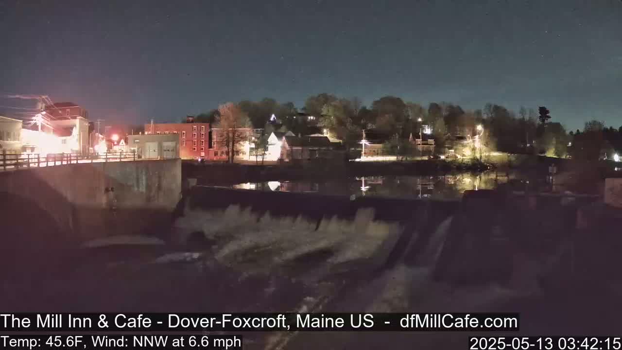 A nighttime view of a town beside a river with a dam, under a clear sky.