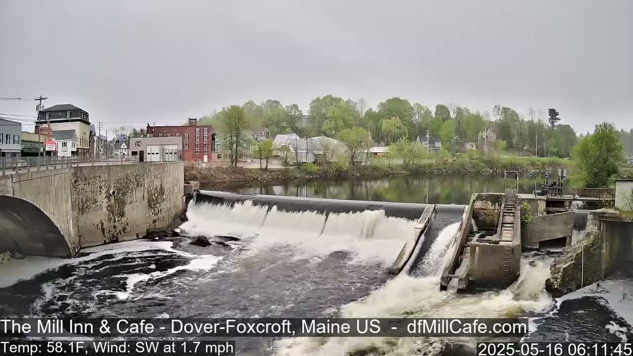 A river flows over a dam in a small town on an overcast day.