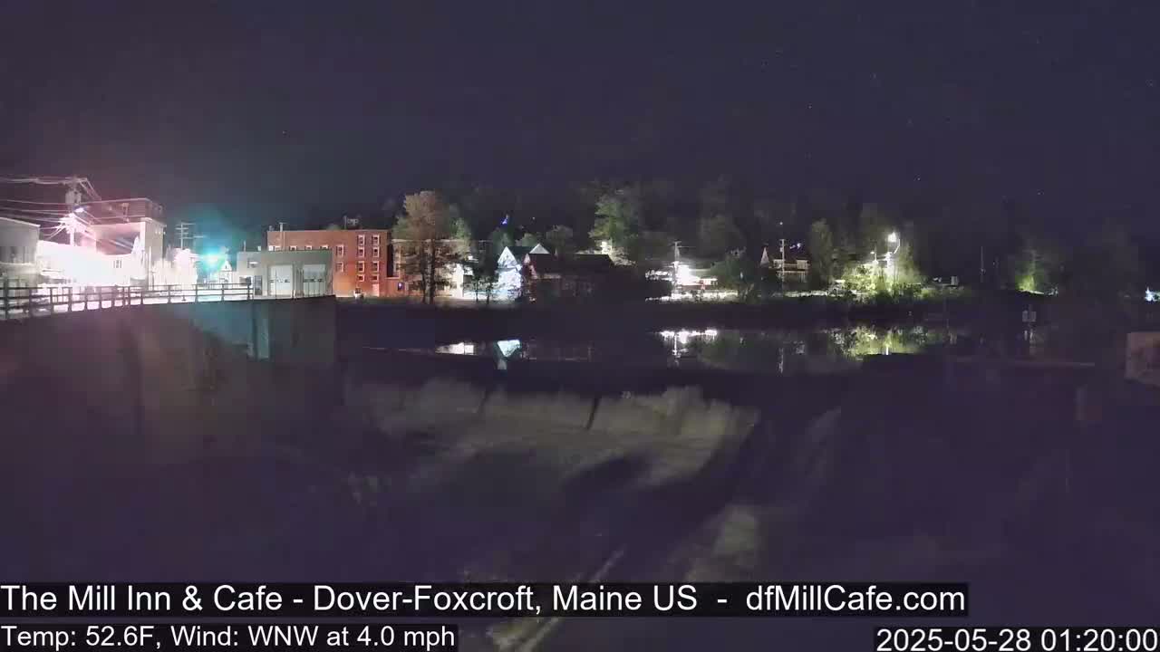 A nighttime view of a town beside a river with a dam, under a clear, starry sky, with a light wind.