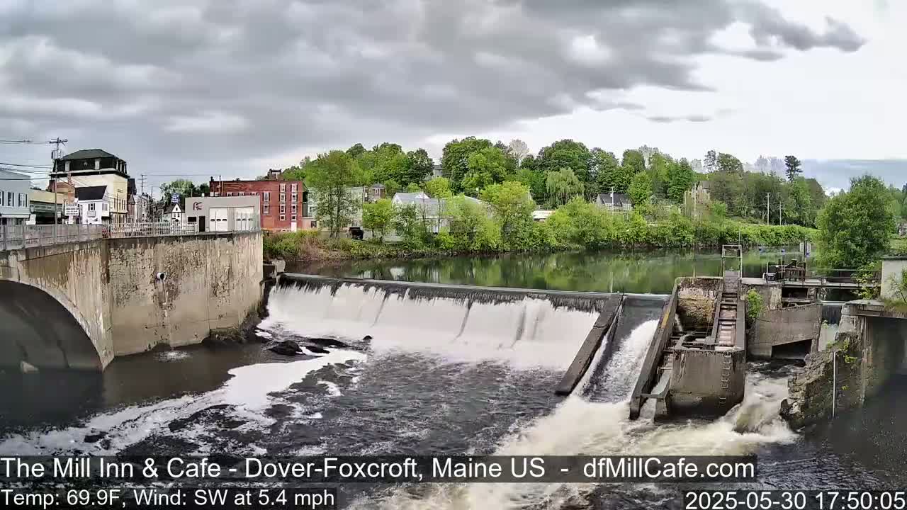 A river flows over a dam next to a town under a cloudy sky.
