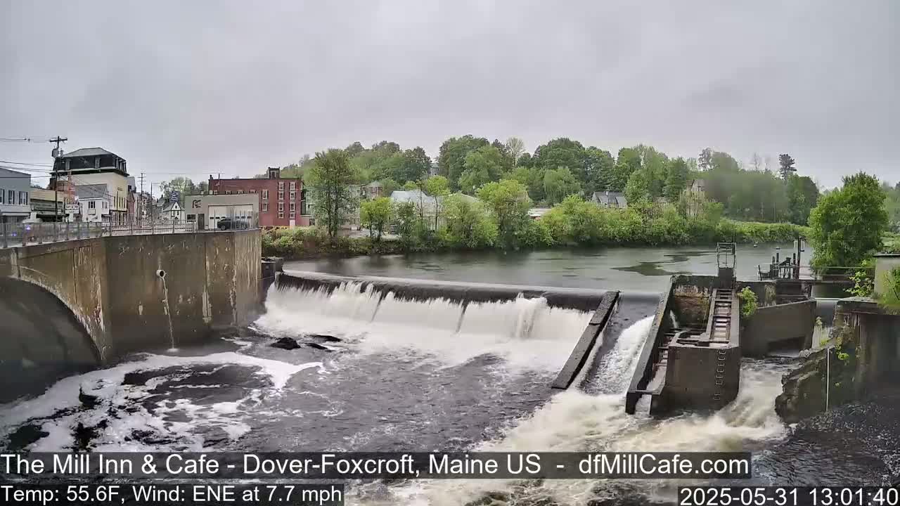 A river flows over a dam in front of a town on an overcast day.