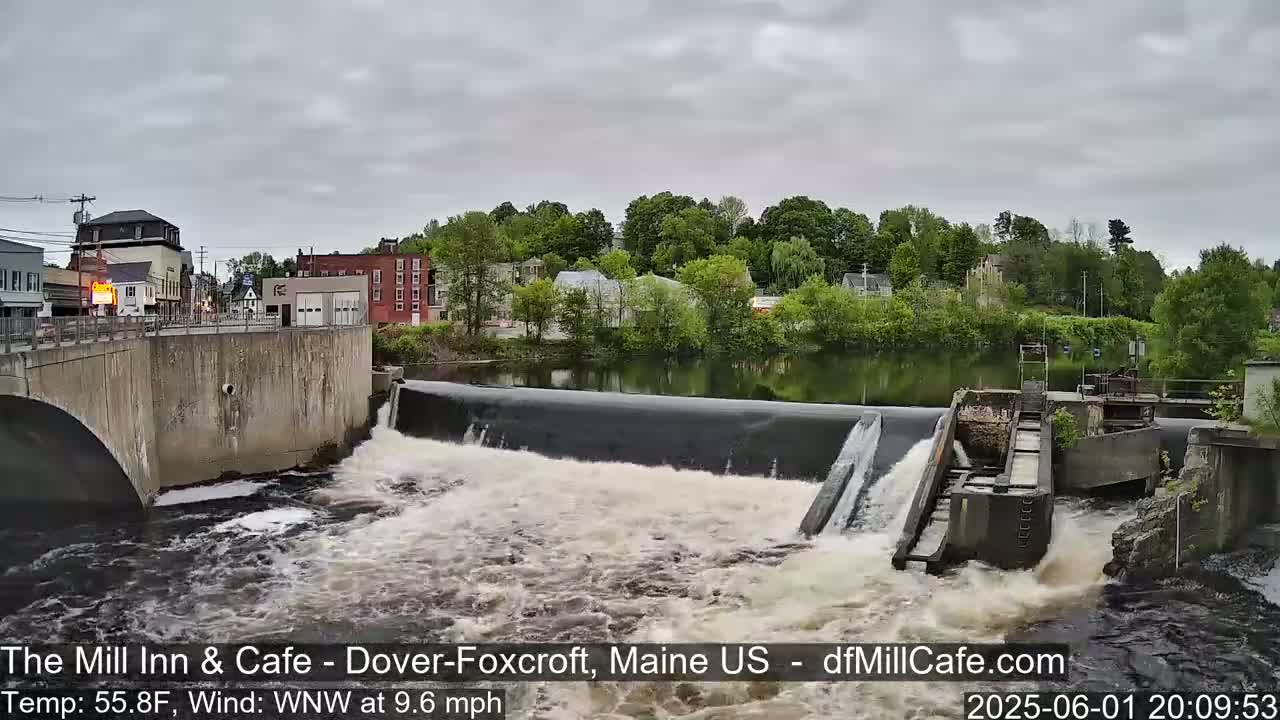 A river flows over a dam under an overcast sky.