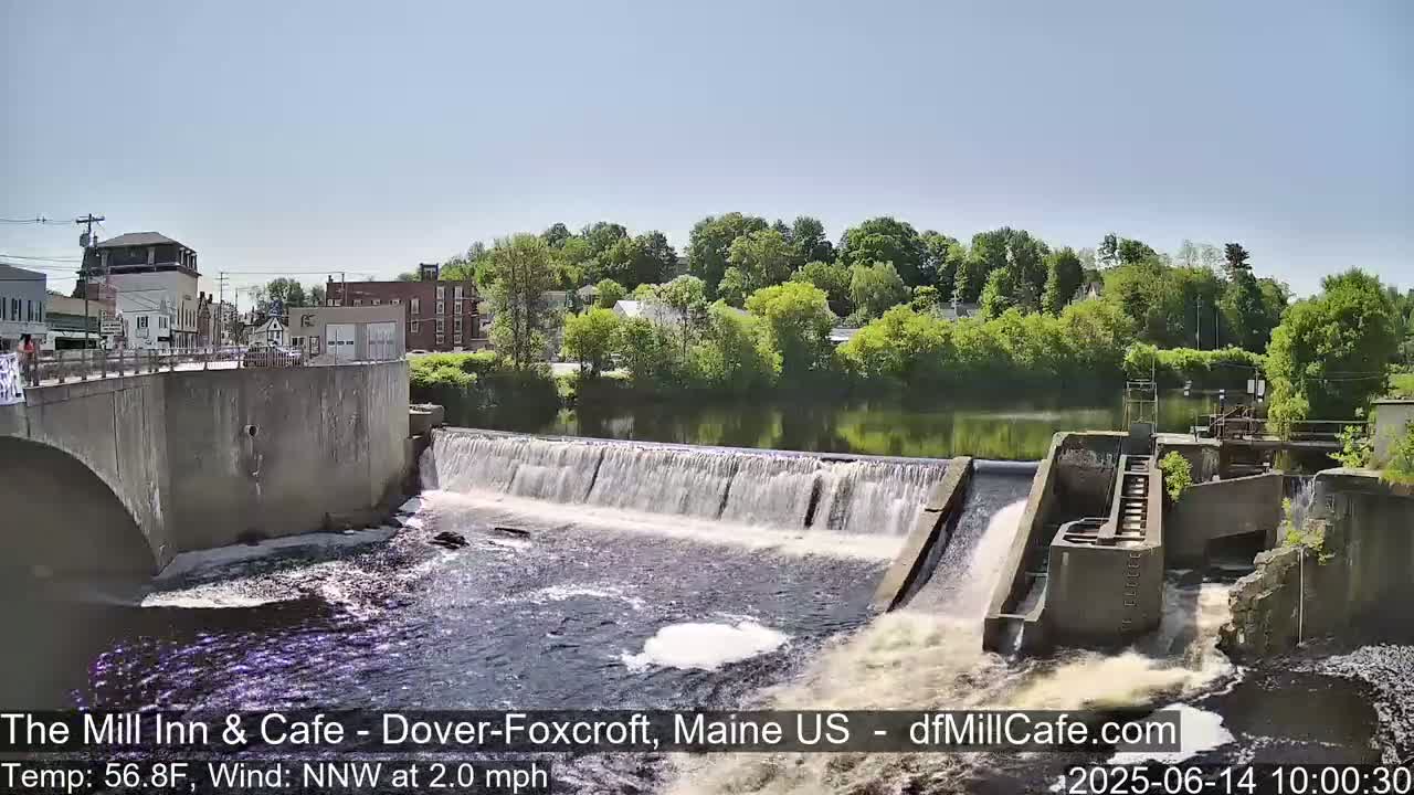 A dam with flowing water is situated next to a town under a clear, sunny sky.