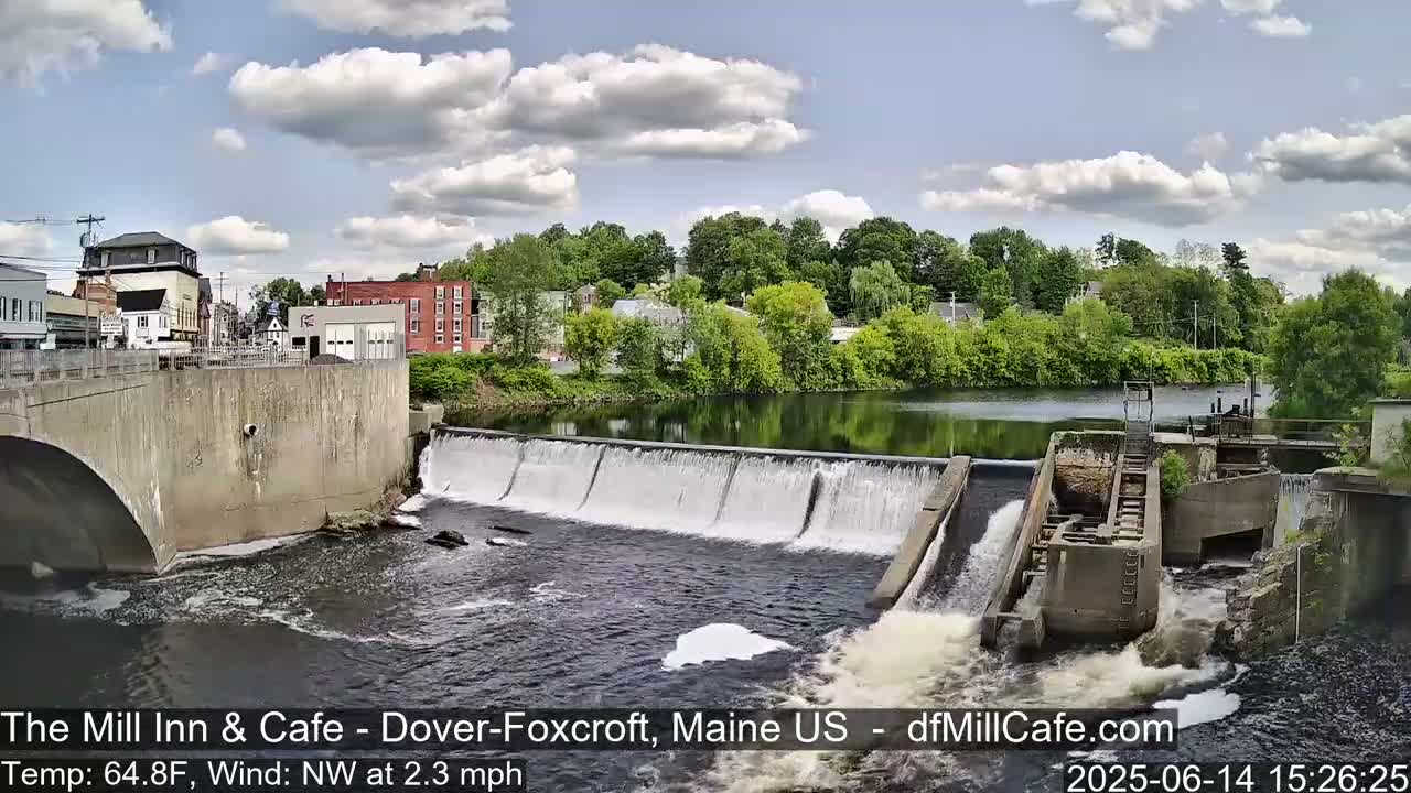 A dam with flowing water is situated next to a town under a clear, sunny sky.