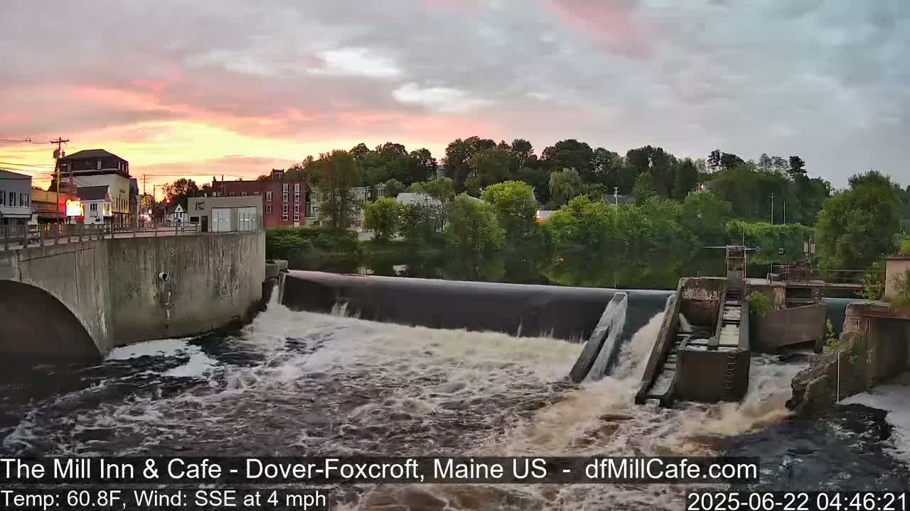 Water rushes over a dam at sunset under a partly cloudy sky.
