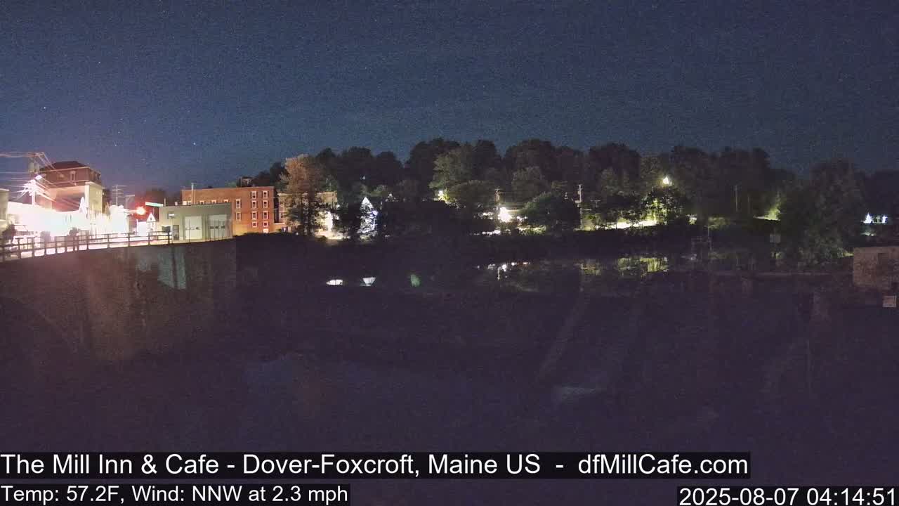A nighttime view of a town by a body of water under a clear, starry sky with a light north-northwest wind.