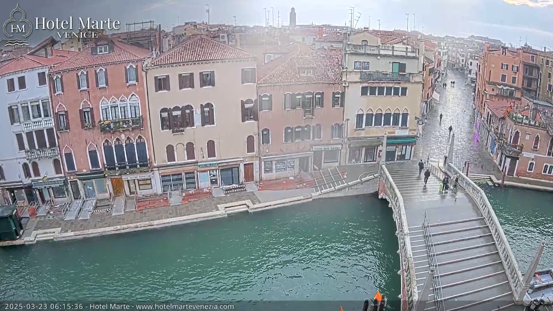 A bridge over a canal in Venice, with several pedestrians on it, is viewed from above on an overcast day.