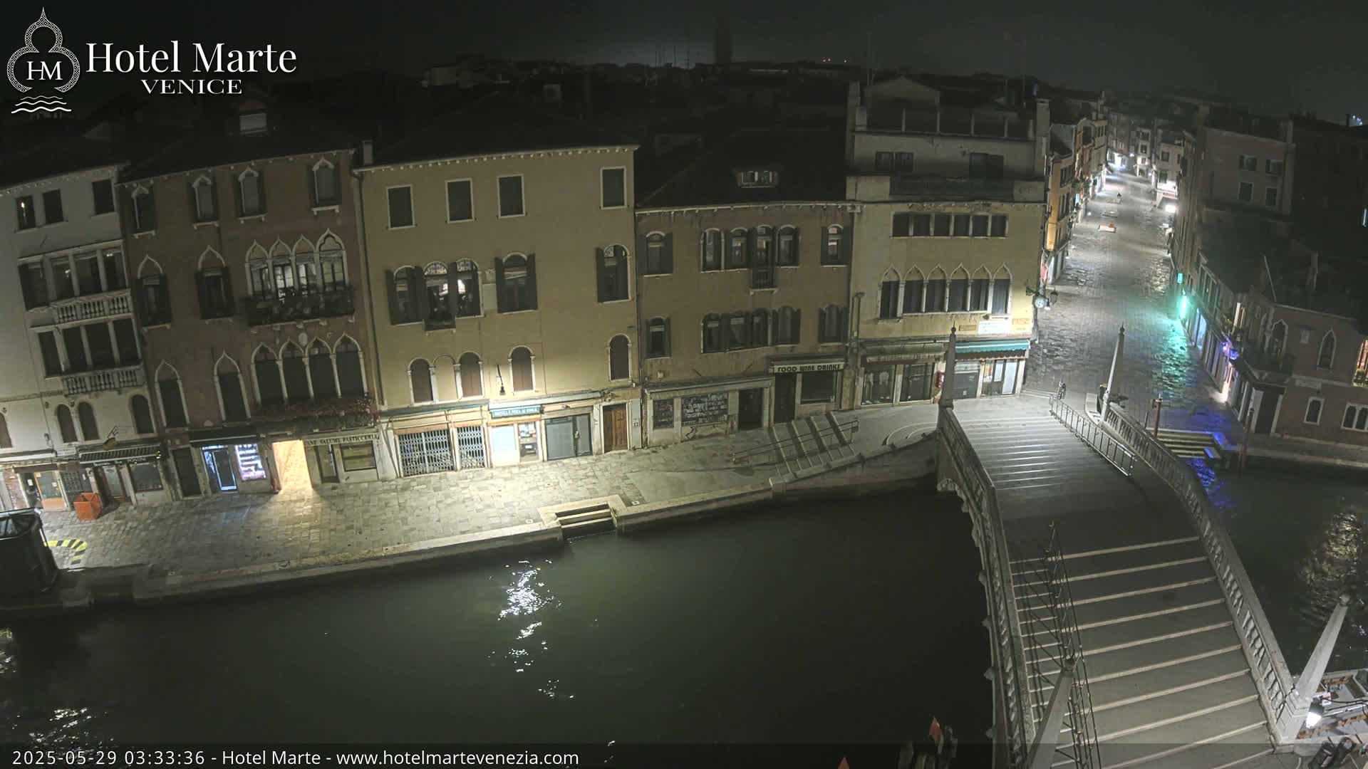 A nighttime, high-angle view of a canal in Venice, showing a bridge and several buildings along the water's edge, with the canal appearing to be slightly flooded.