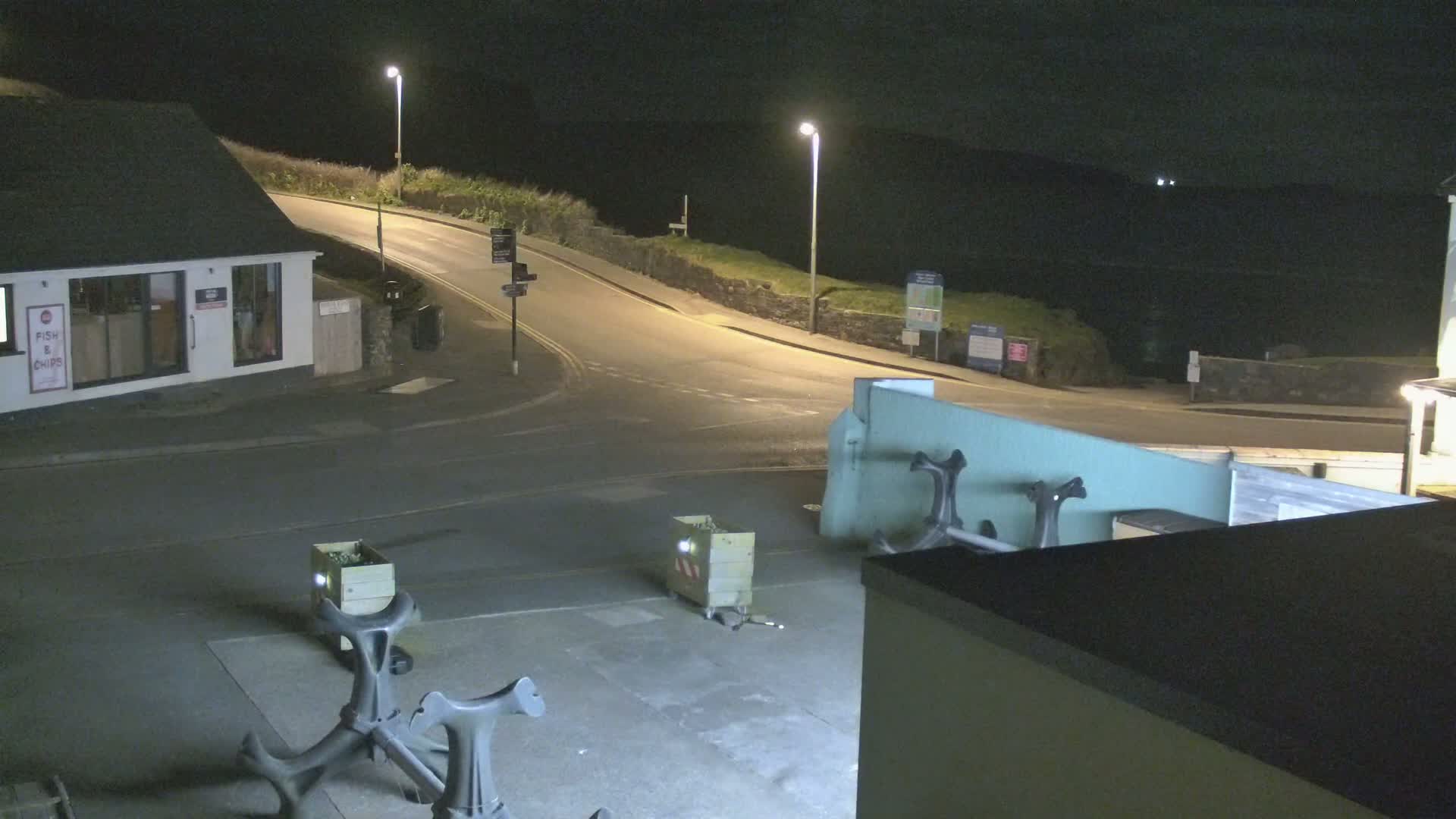 At night, a street corner with a fish and chips shop and two metal anchors is illuminated by streetlights.