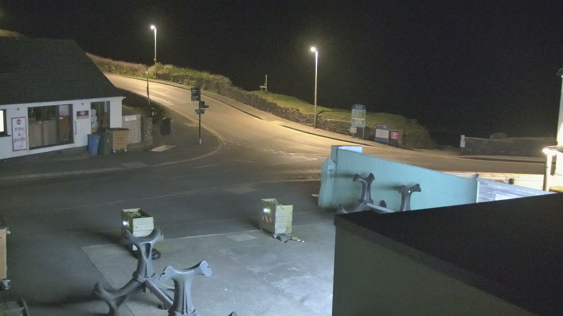 At night, a street corner with a fish and chips shop and several crates is illuminated by streetlights.