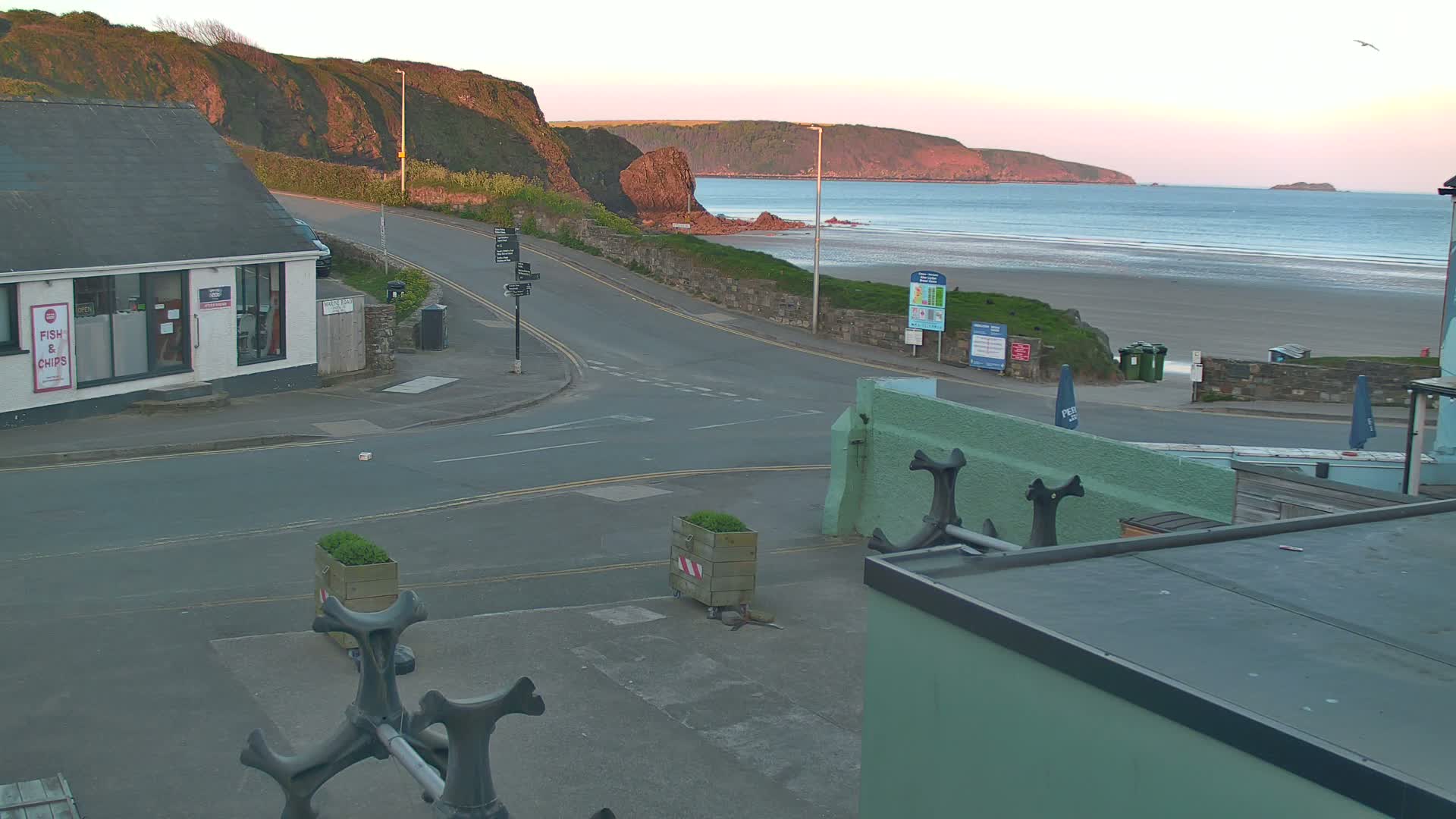 A seaside town scene at dawn shows a sandy beach with gentle waves, a road leading down to it, and a building with a "fish & chips" sign.