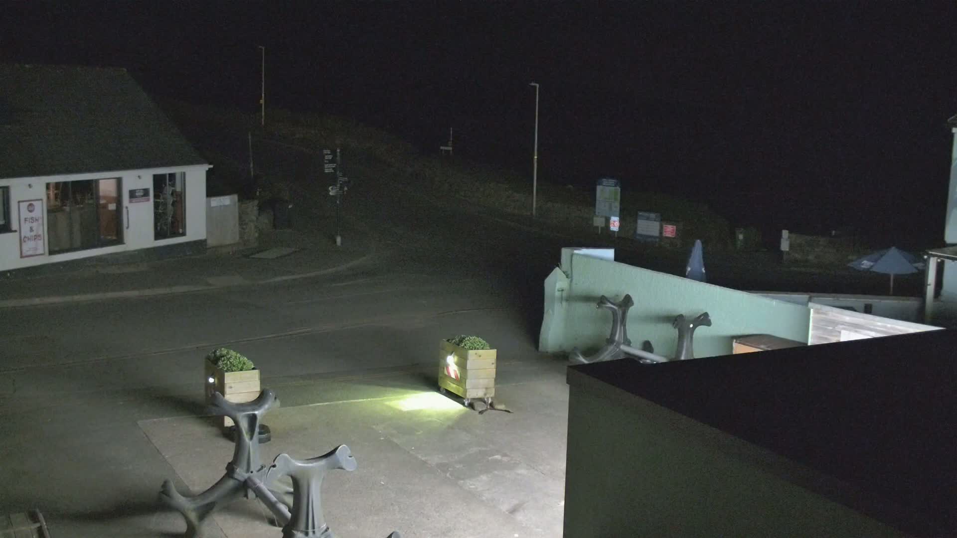 At night, a brightly lit area shows several dark-colored anchors on the ground near a small building and a street.