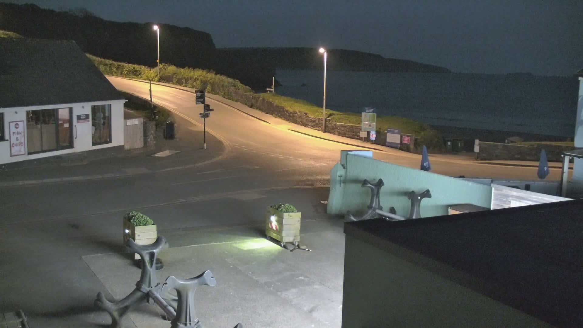 At night, a coastal road curves around a building near a dark body of water under artificial light.