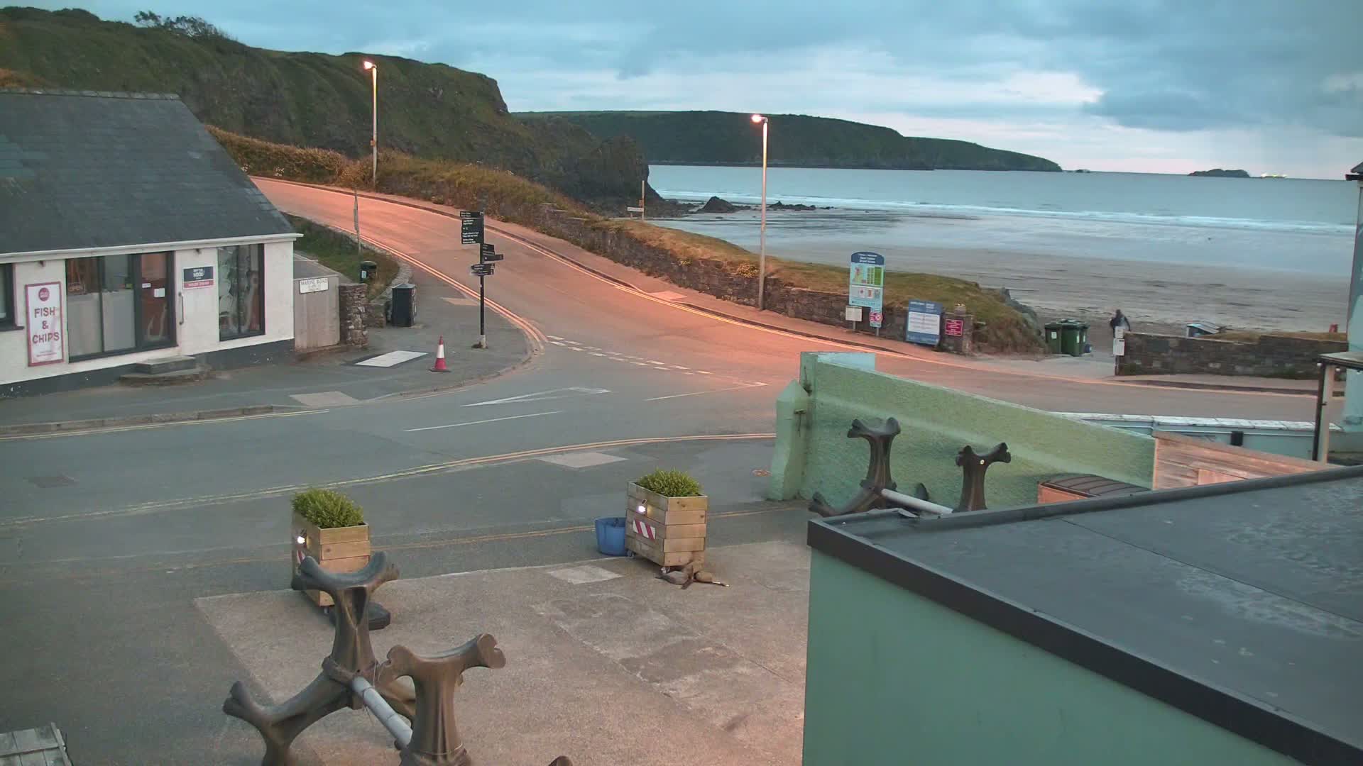 A coastal road curves toward a sandy beach under a cloudy, twilight sky.