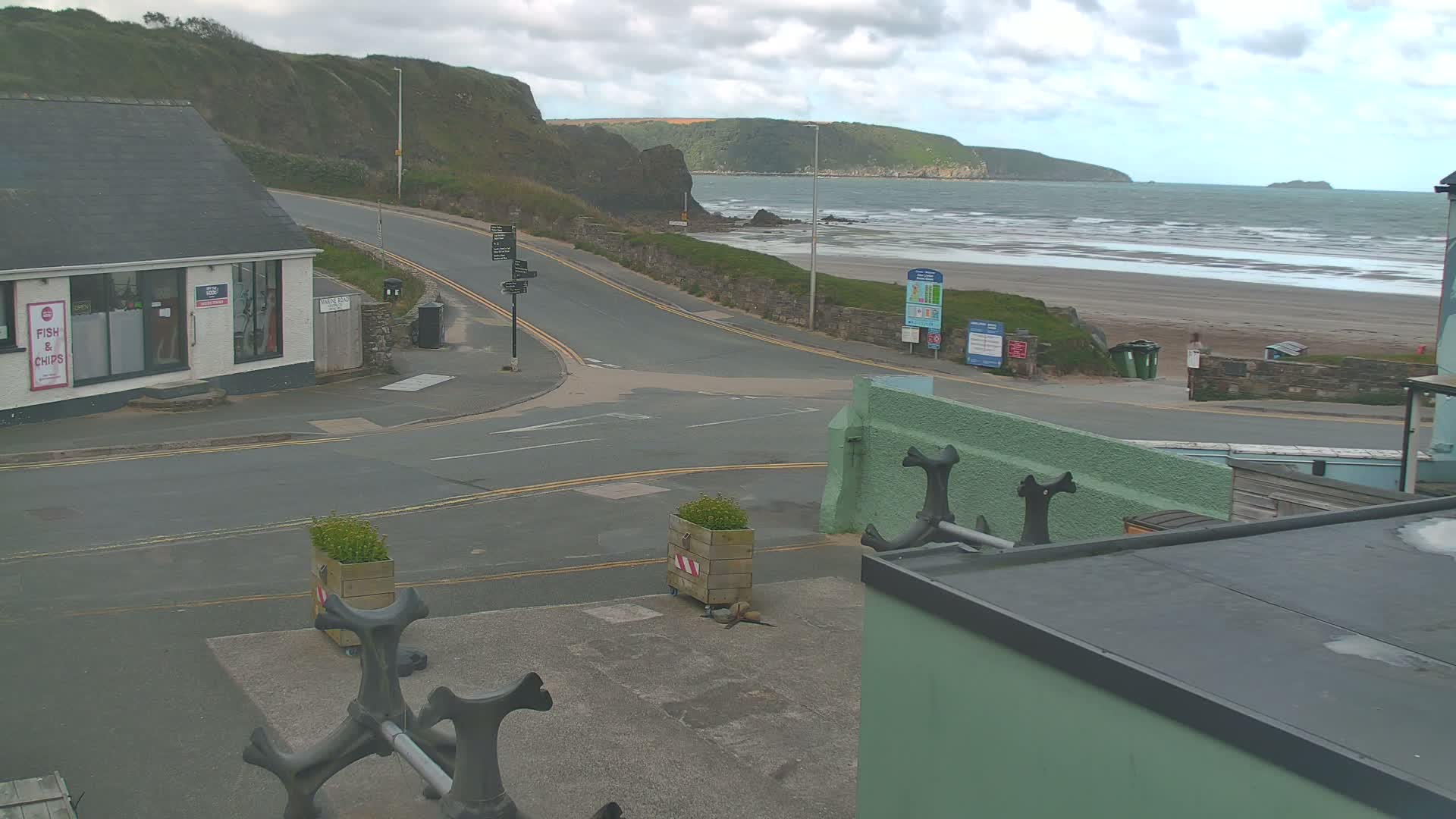 A coastal road intersection overlooks a sandy beach with wavy ocean under a cloudy sky.