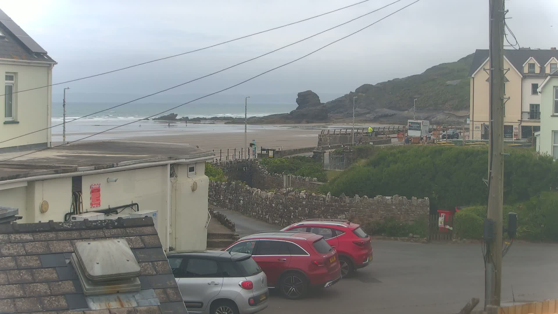 Three red cars are parked in a lot overlooking a sandy beach with small waves under an overcast sky.