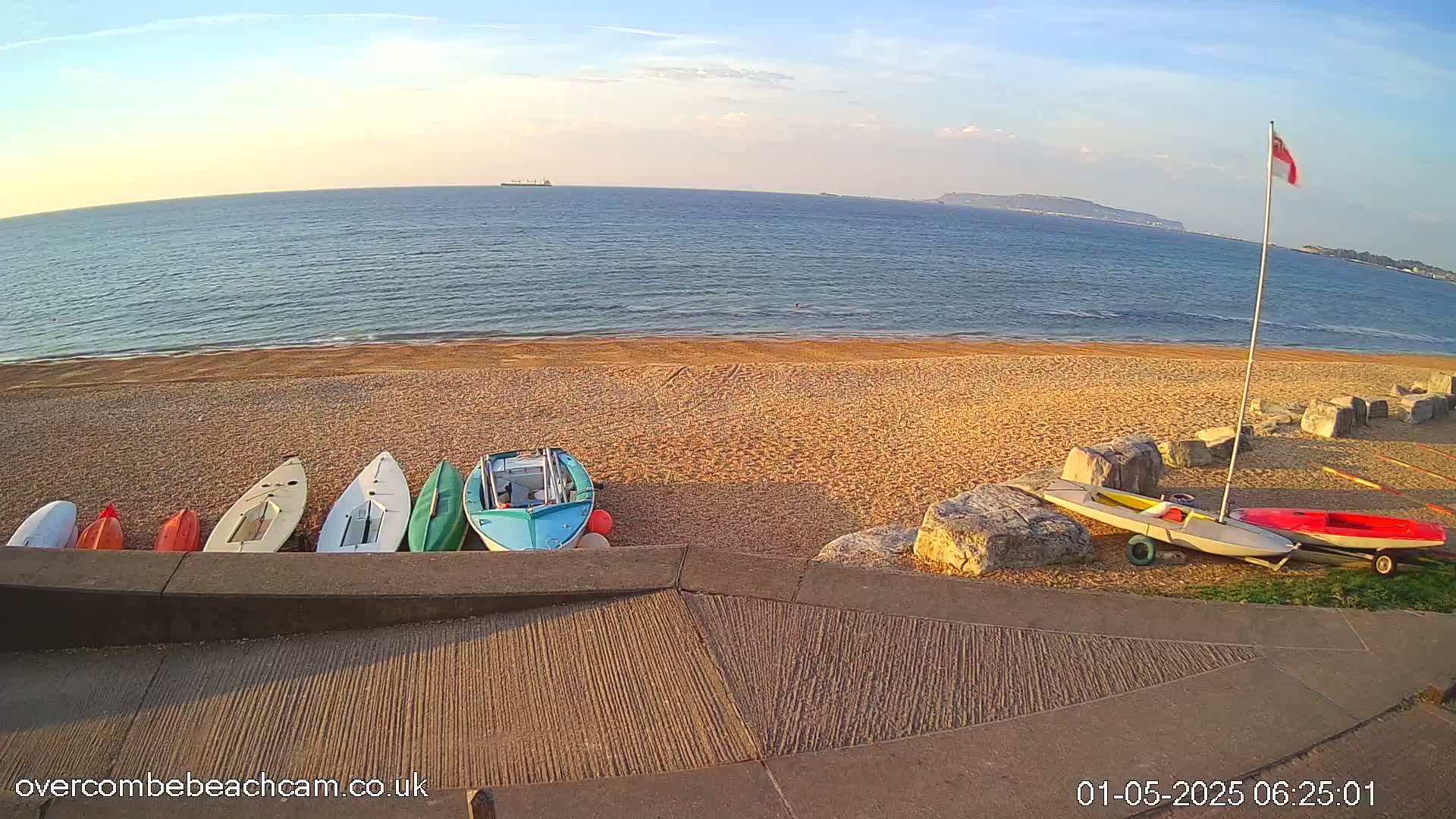 Several small boats are resting on a sandy beach next to calm, blue water under a clear sky.