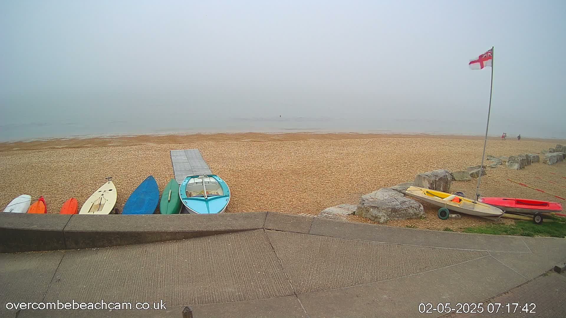 Several small boats and kayaks are lined up on a sandy beach next to a calm, foggy sea.