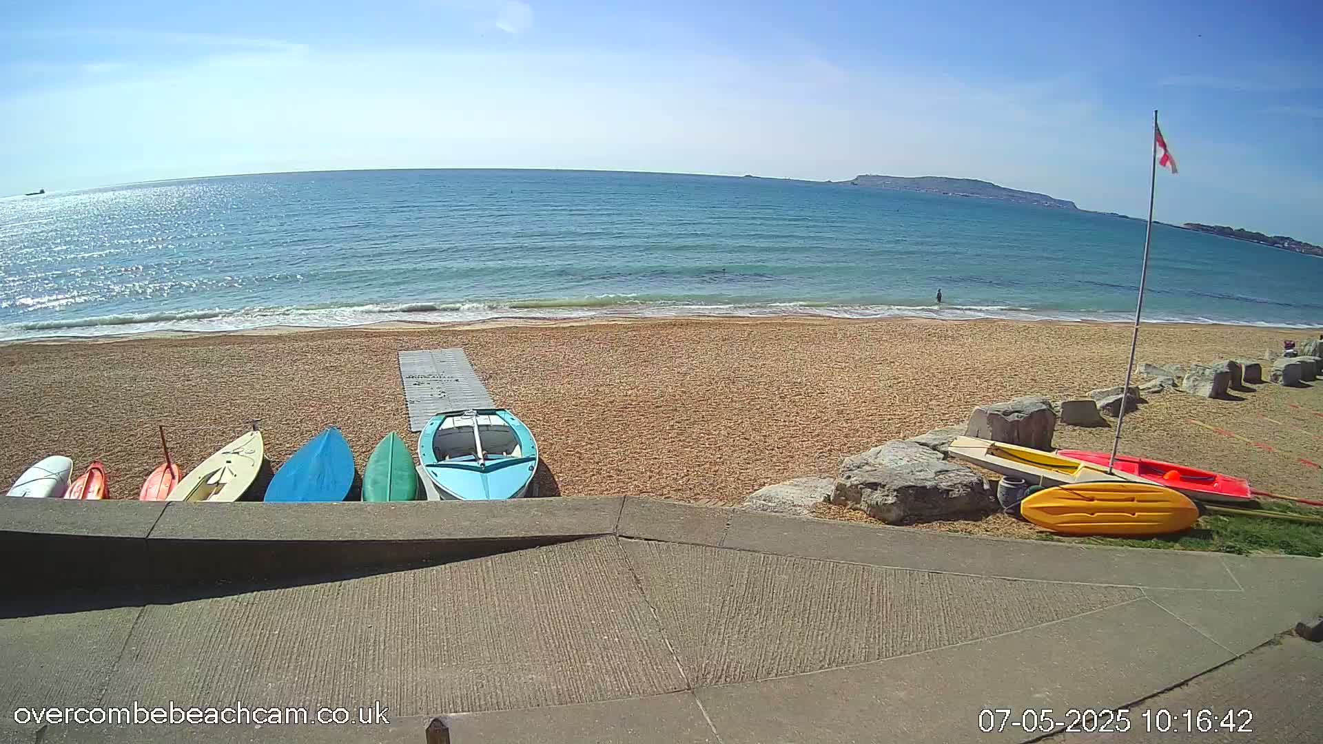 Several small boats are lined up on a sandy beach next to a calm, sunny ocean.