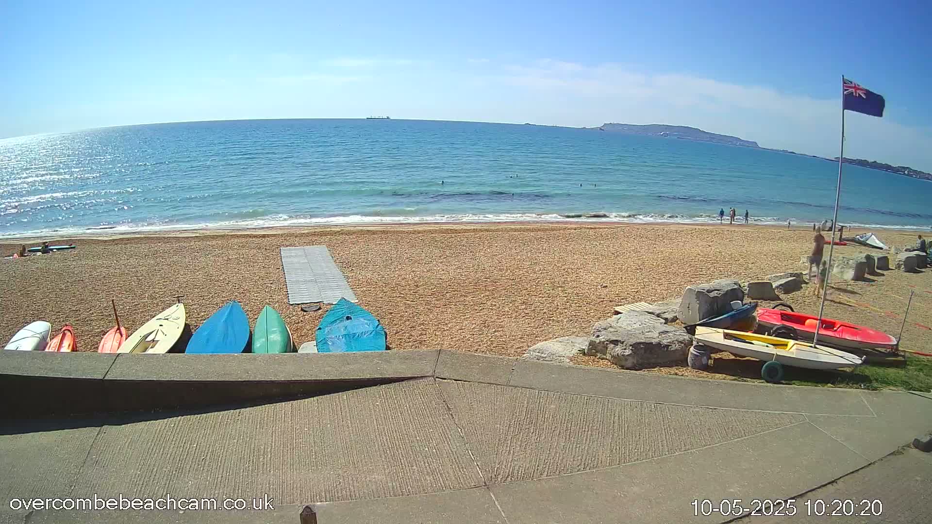 A sandy beach with several small boats and kayaks near the water's edge, under a clear blue sky on a sunny day.