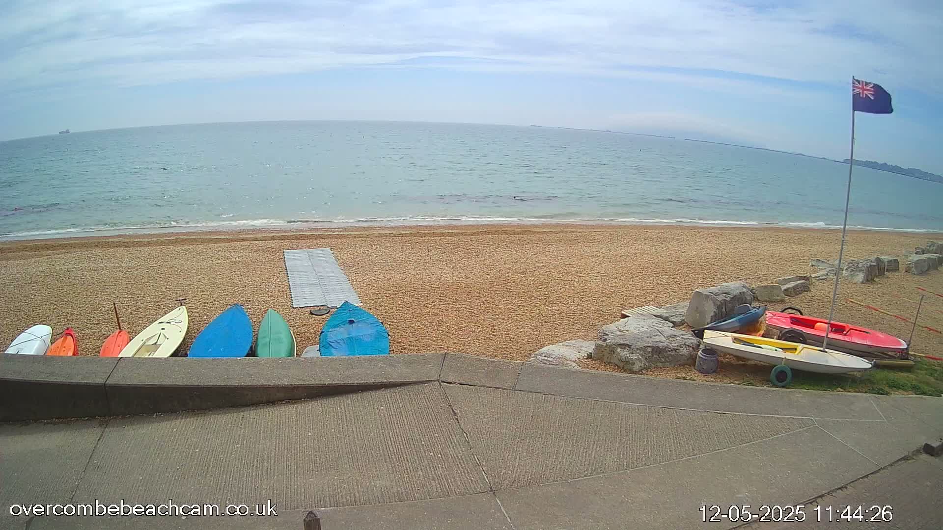 Several small boats are lined up on a sandy beach next to a calm sea under a partly cloudy sky.
