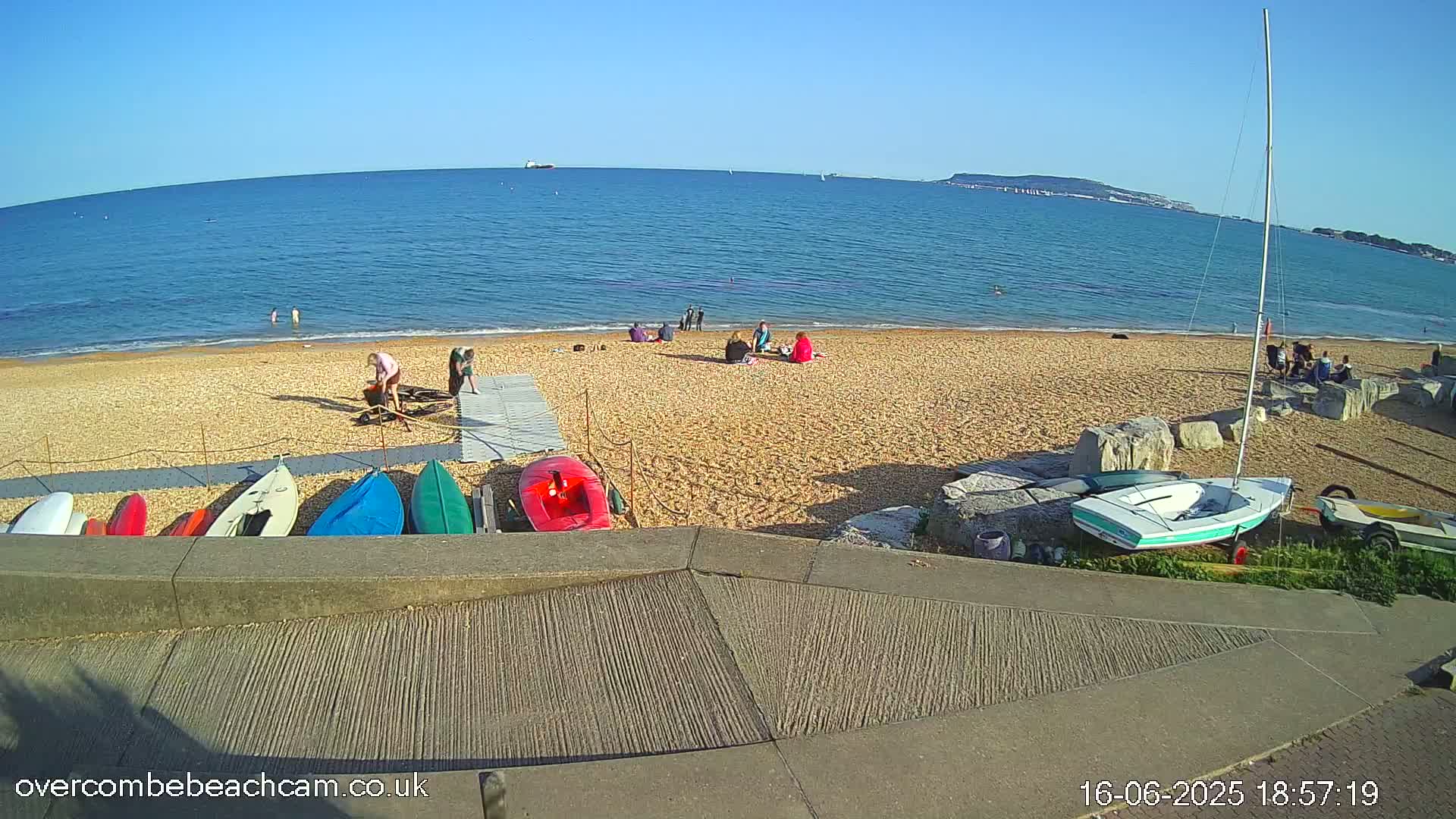 A sandy beach with several people relaxing and some kayaks and sailboats on a sunny day with a calm ocean in the background.