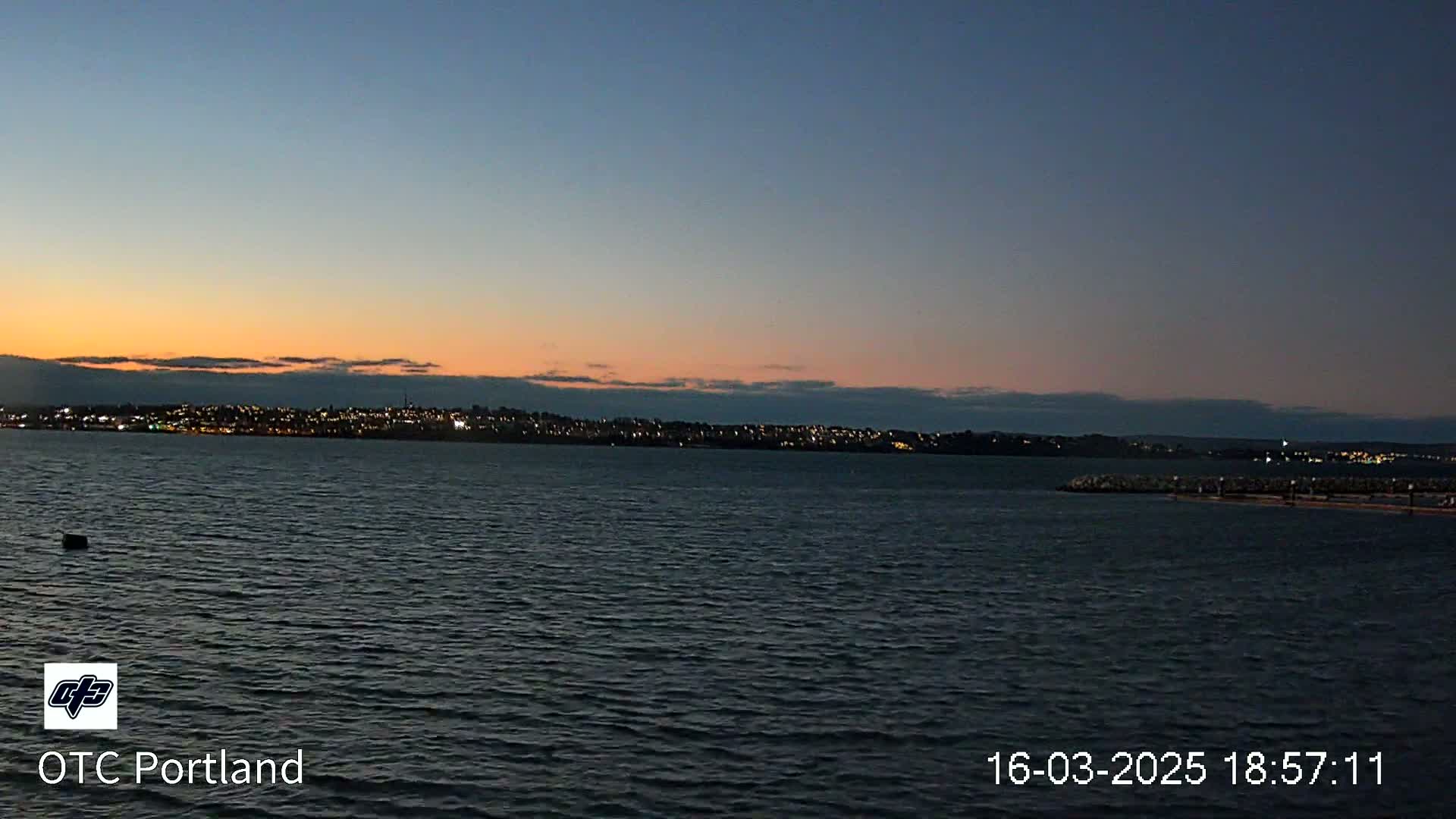A calm body of water shows a city skyline at dusk under a clear, twilight sky.