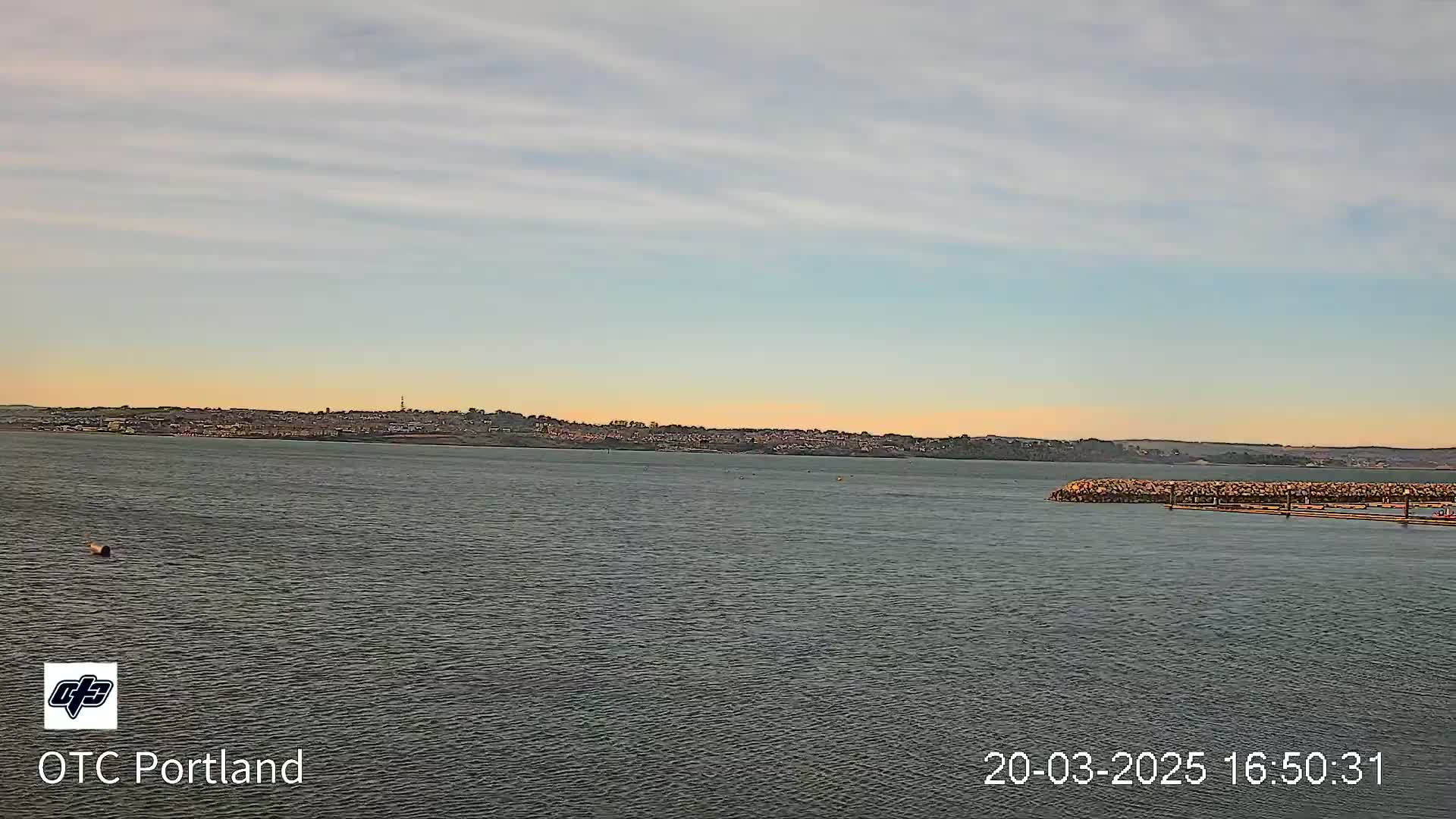 A calm body of water shows a distant shoreline under a partly cloudy, sunset sky.
