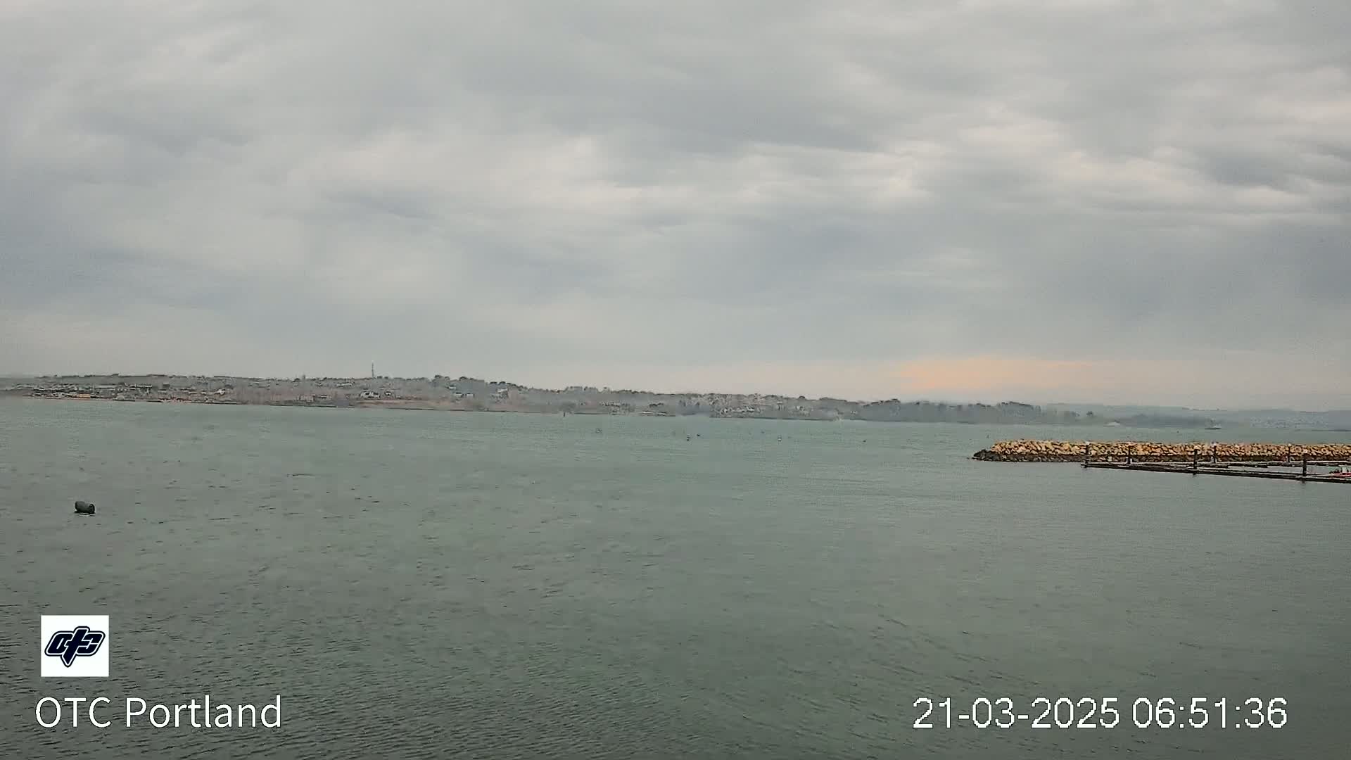 A calm body of water stretches out to a distant shoreline under an overcast sky.