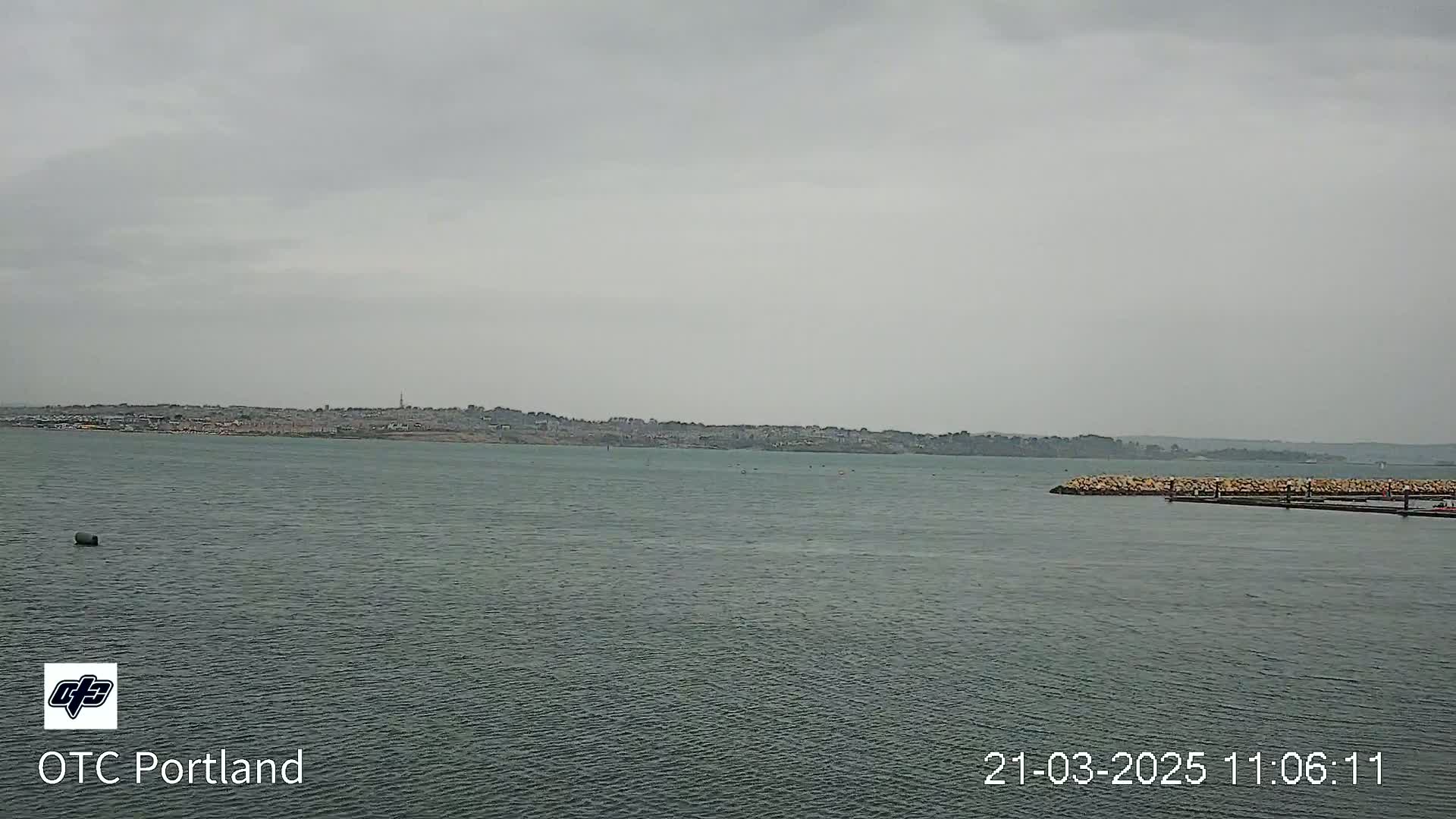 A calm body of water stretches out to a distant shoreline under an overcast sky.