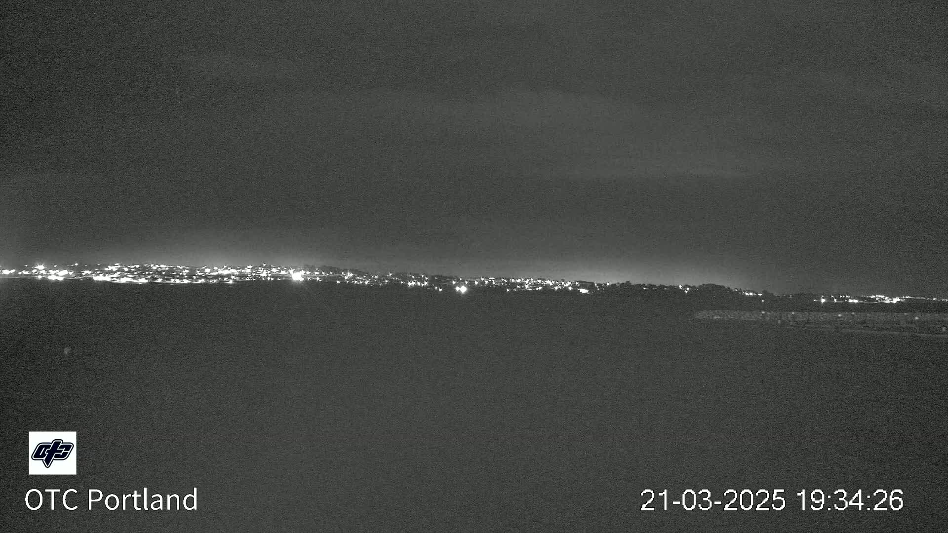 A nighttime long shot shows a city skyline on the horizon under a dark, cloudy sky.